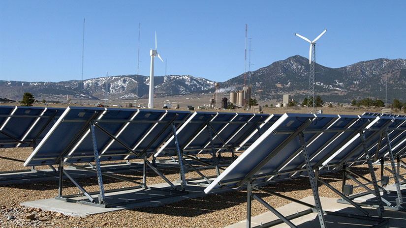 Solar panel array with wind turbines in the background