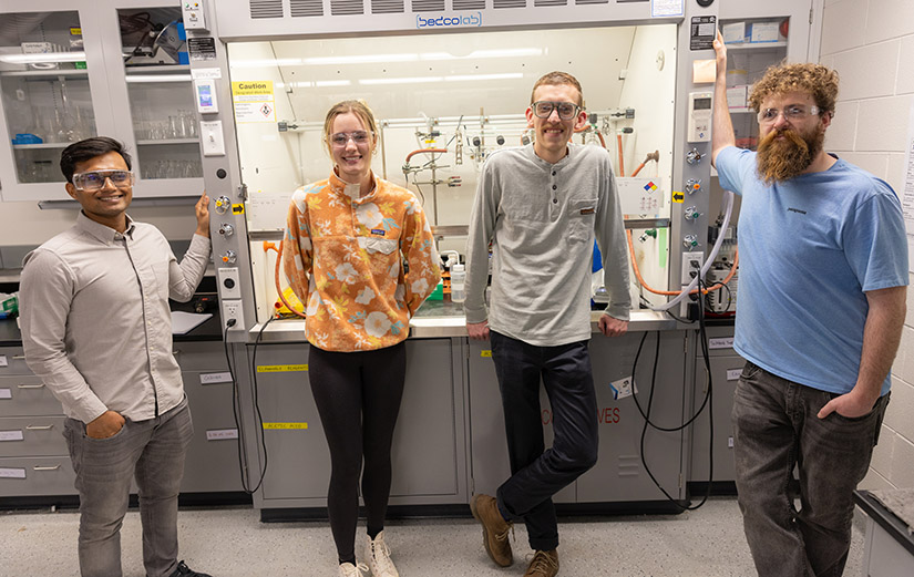 Four people stand in front of laboratory equipment.