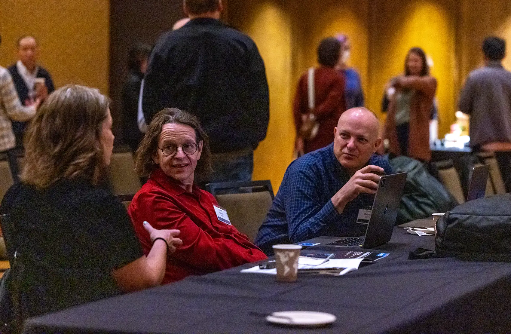 20250814-100383 Three attendees engage in focused discussion while sitting at a table in the workshop hall.
