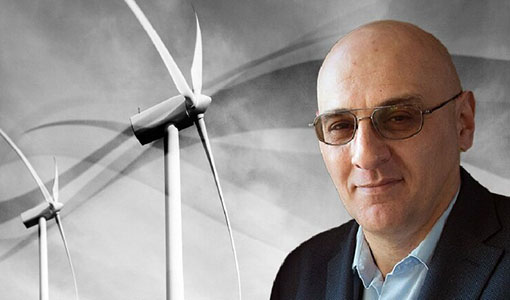 behind-the-blades-vahan Vahan Gevorgian in sunglasses standing in front of solar photovoltaic panels and a wind turbine