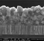 Black-and-white cross-section image of two-layer material showing lower layer with regular vertical  columnar crystallization and thicker upper layer with more coarsely crystalline material having an irregular surface geometry.